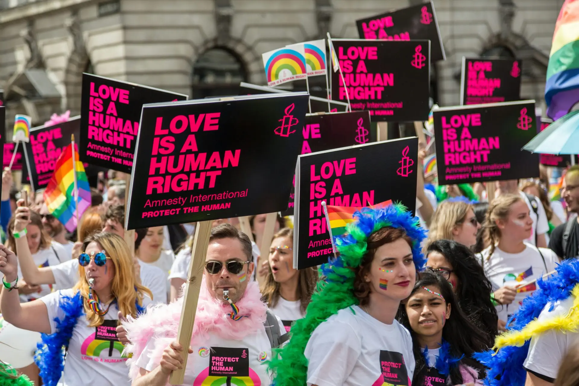 Manifestation LGBTQ+ avec des pancartes Amnesty International affichant le message 'Love is a human right', des drapeaux arc-en-ciel et des participant·es portant des t-shirts militants.